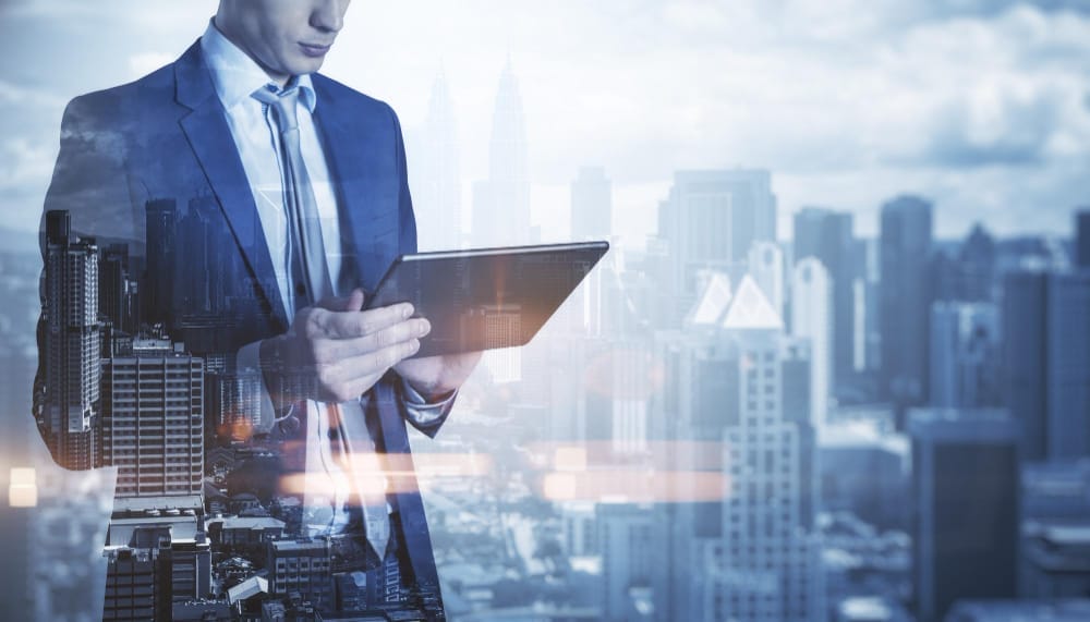 Business professional in a suit holding a tablet, with a cityscape in the background, creating a double exposure effect that blends the individual with the urban environment, symbolizing the integration of technology and business in a modern city setting.